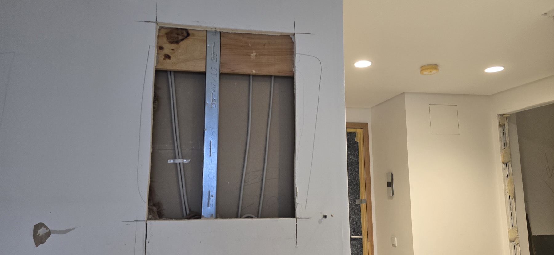 Aufgeschnittene Trockenbauwand mit freigelegten Versorgungs­leitungen und sichtbarer Wasserspur am Wandfuß — Europaallee Wohnung H 07-07