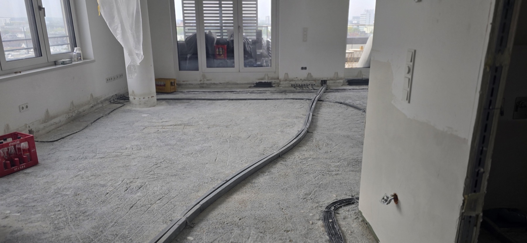 Leere Wohnung im Rohzustand mit Beton-Untergrund und Blick auf die Frankfurter Skyline durch große Balkonfenster