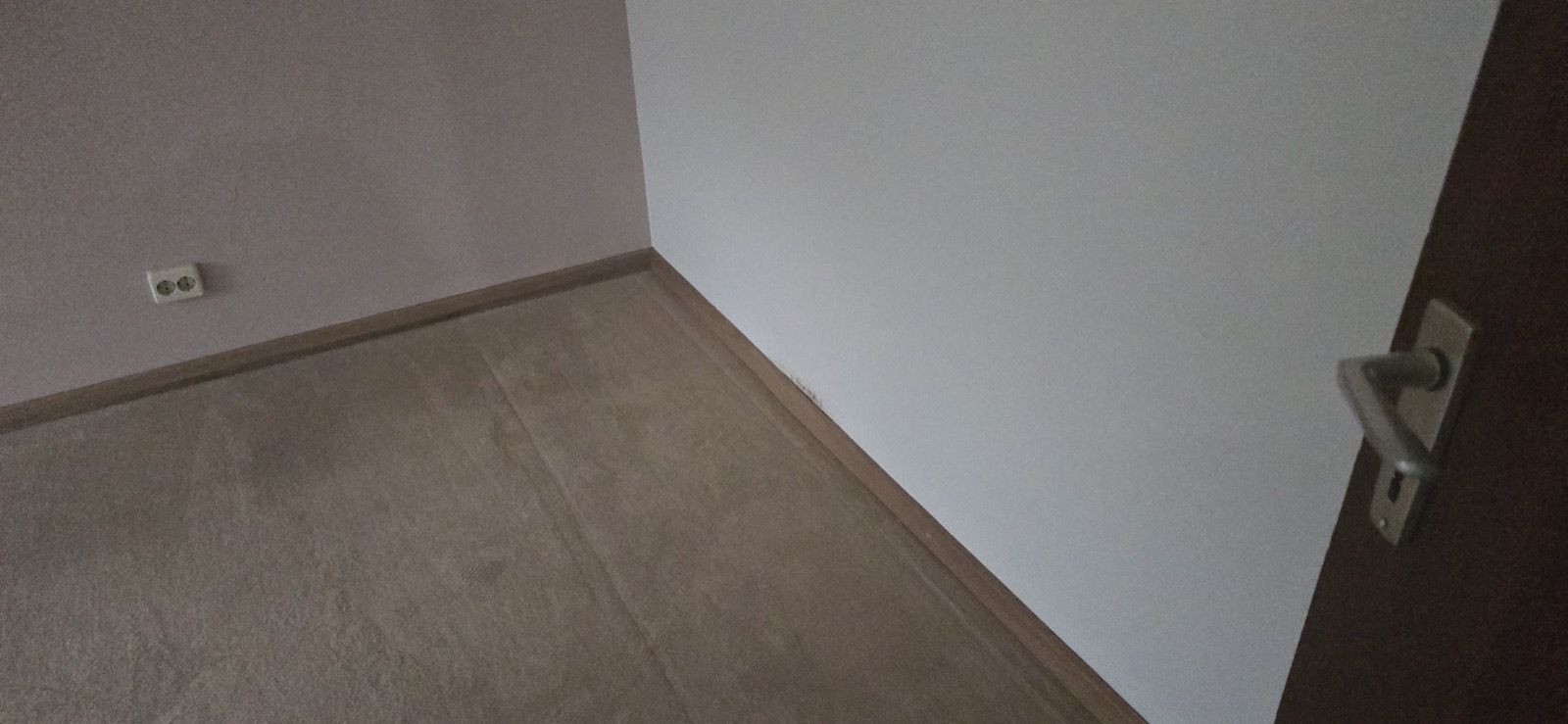 Zimmerecke mit altem beigem Teppichboden, dunklem Türrahmen und blau gestrichener Wand vor der Sanierung — Hubertushöhe 8