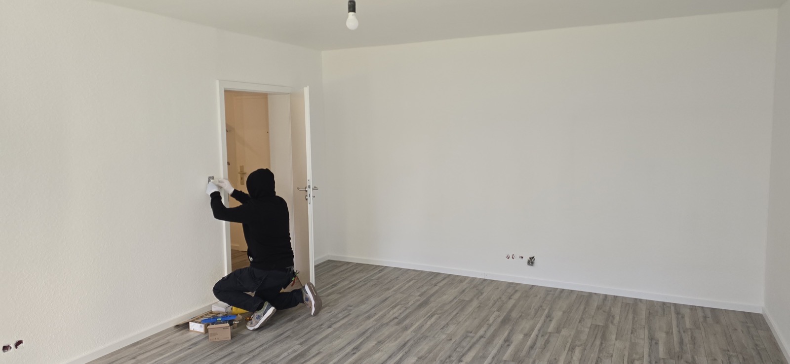 Fertig sanierter heller Raum mit grauem Vinyl-Designboden und Handwerker beim Setzen einer Steckdose — Hubertushöhe 8